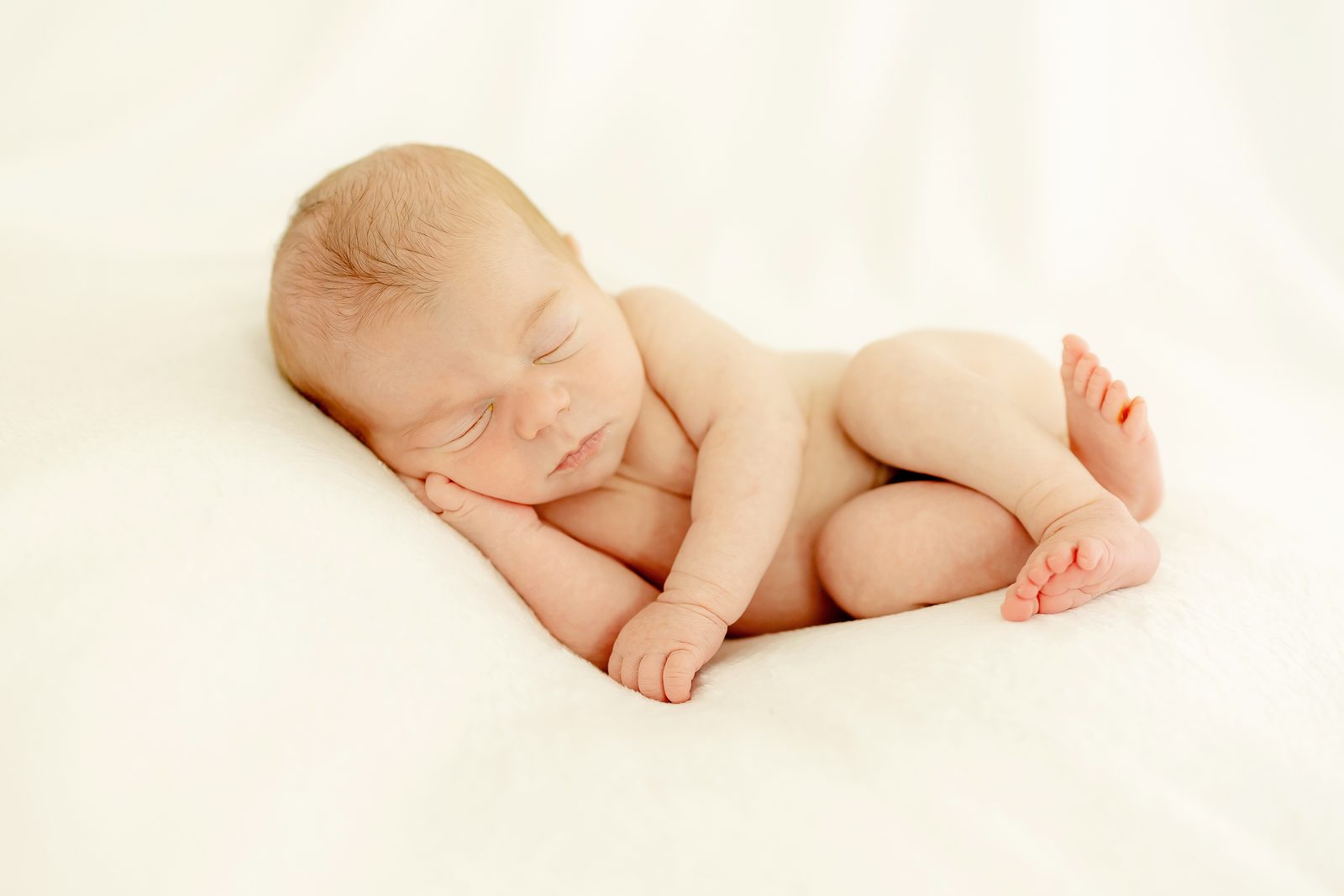 Naked newborn sleeping peacefully on a cream blanket