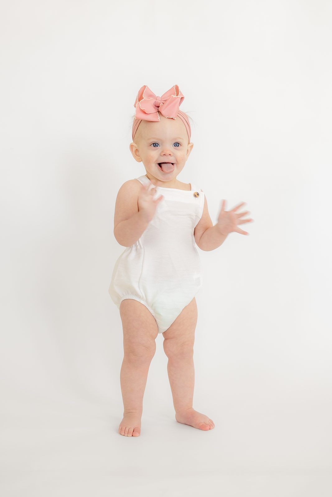 One-year-old standing in white romper with pink bow